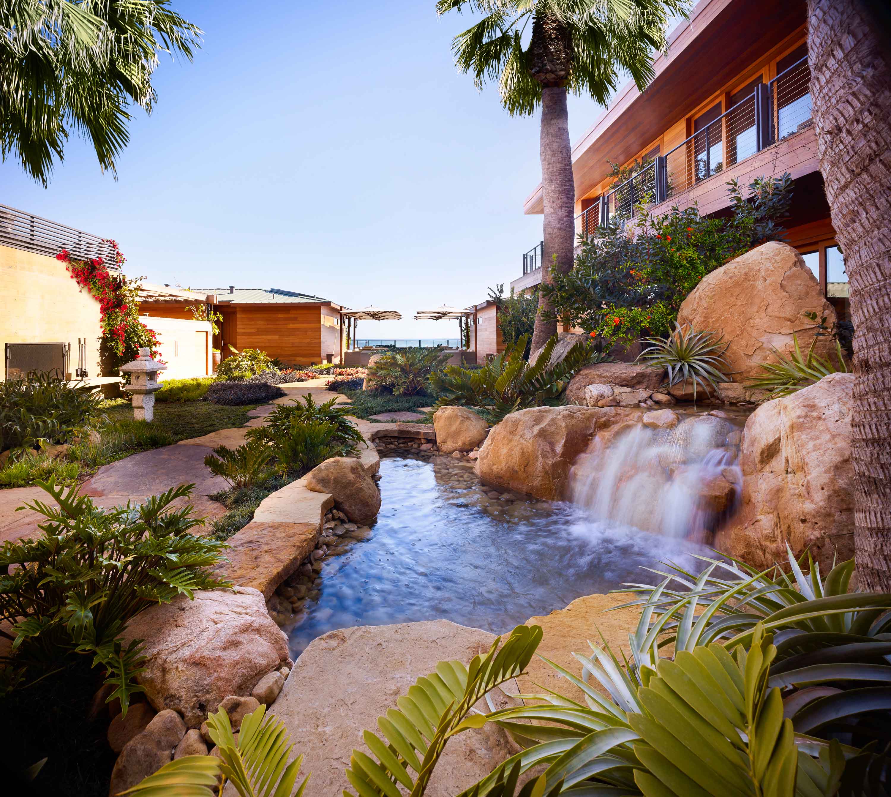 Ocean view courtyard of Nobu Ryokan Malibu with waterfall pond, exterior of the building and palm trees